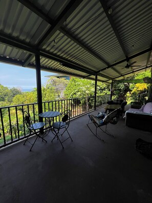 A covered outdoor area with a table and chairs, a sofa, and a railing overlooking a lush landscape. - Amazing Ocean view guest house, just next to a monkey trail (Guanacaste Province)