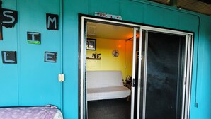 Una habitación color aguamarina con un ventanal corredero que da a un interior amarillo. Hay una cama con un cubrecolcha estampado y una silla con un cubrecolcha púrpura.