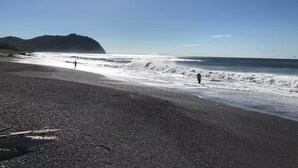 Una playa con orilla de guijarros, olas y una montaña al fondo.