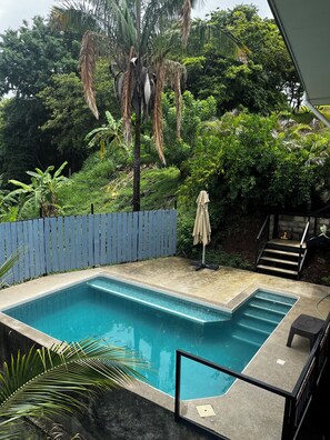 A rectangular swimming pool with a tiled edge, surrounded by a wooden fence and lush greenery. - Amazing Ocean view guest house, just next to a monkey trail (Guanacaste Province)