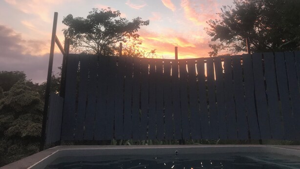 Una valla de madera con árboles al fondo y un atardecer en el cielo.