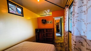 Una habitación con cama, ventilador, ventana con cortinas y puerta que da a otra habitación.