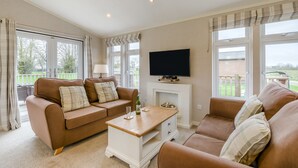 Ein Wohnzimmer mit braunem Sofa, Couchtisch, Flachbildfernseher und großen Fenstern.