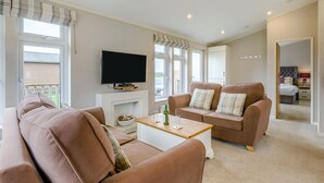 Ein Wohnzimmer mit Sofa, Couchtisch, Fernseher und einem Fenster mit Vorhängen.