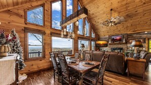 Un interior rústico de madera con comedor, chimenea y ventanas amplias que ofrecen vistas panorámicas.