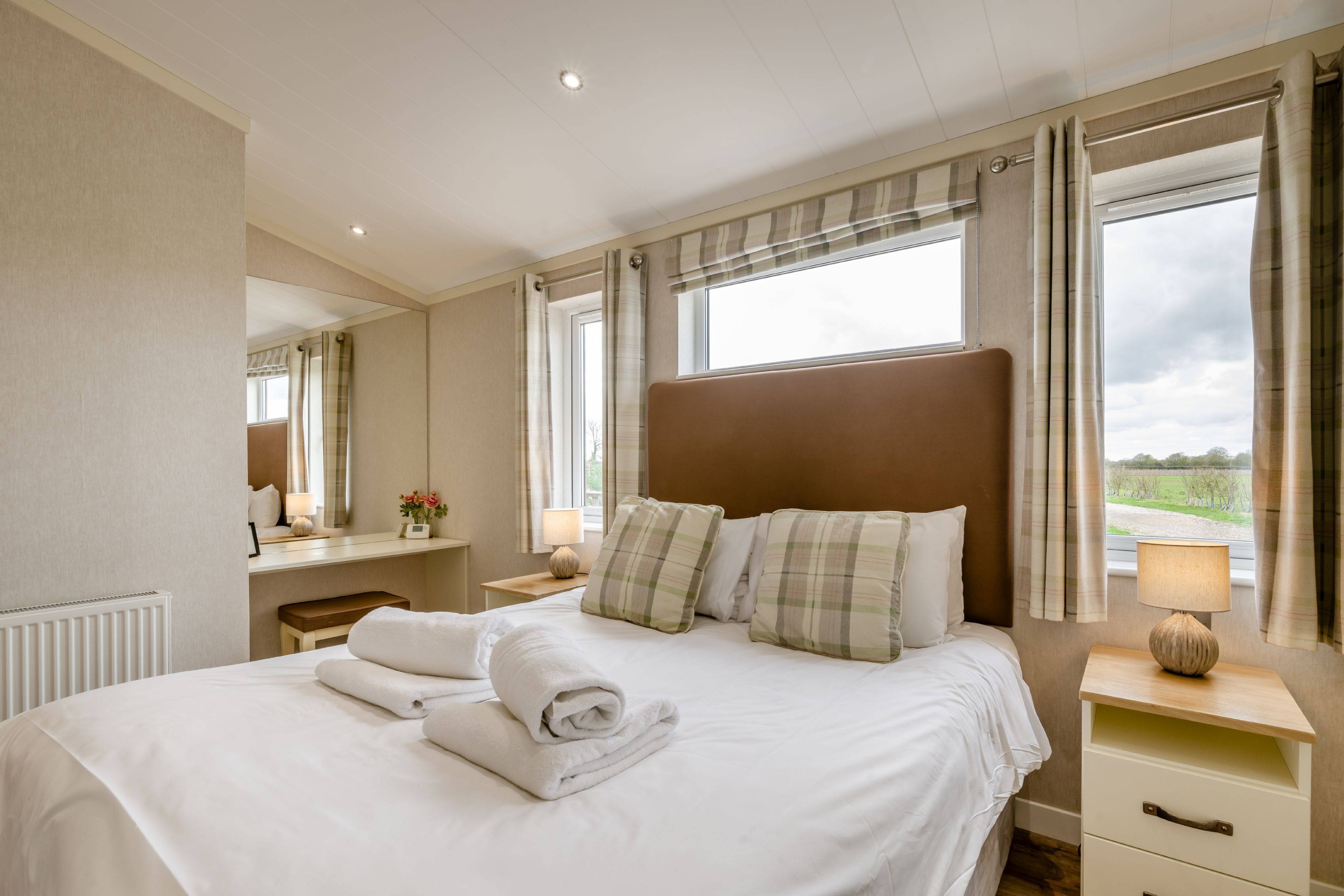 Une chambre d’hôtel avec un grand lit, une table de chevet, une lampe, un miroir et une fenêtre avec des rideaux.