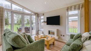 Een woonkamer met een groene bank, een houten salontafel, een flatscreen televisie en een open haard.