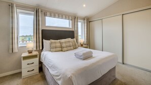 Een slaapkamer met een bed, nachtkastjes, een raam met gordijnen, een nachtkastje en een kledingkast.