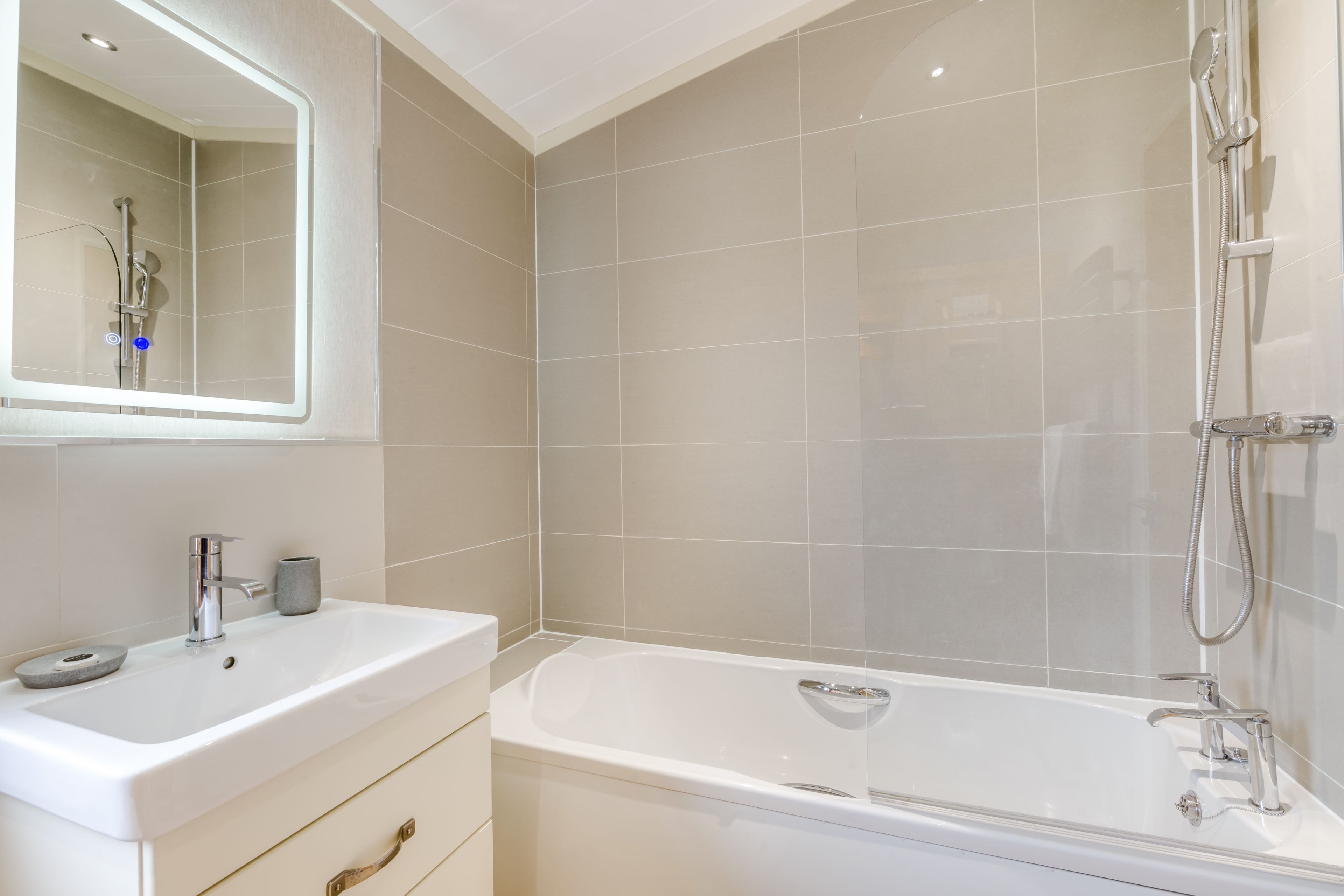 Un baño moderno con lavamanos, espejo y bañera blancos.