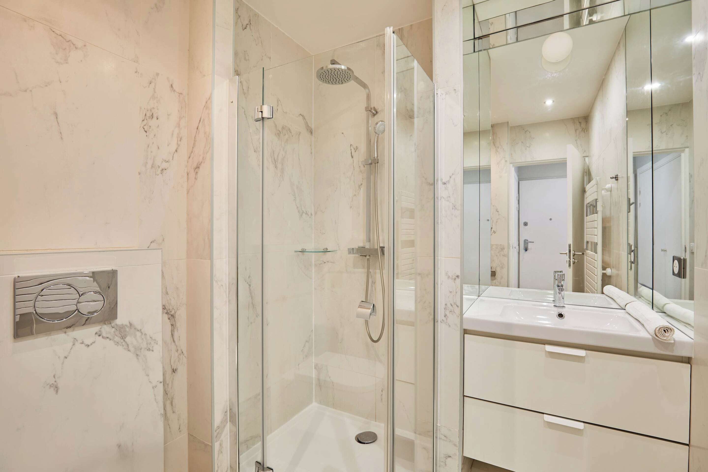 A modern bathroom with a glass-enclosed shower, a large mirror, and a white sink.