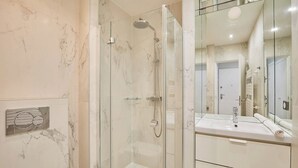 A modern bathroom with a glass-enclosed shower, a marble-tiled wall, and a large mirror above a white sink. - Modern Suite Invalides Tour Eiffel (Paris)