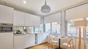 A modern kitchen with white cabinets, a built-in oven, and a dining area with a table and chairs. - Modern Suite Invalides Tour Eiffel (Paris)