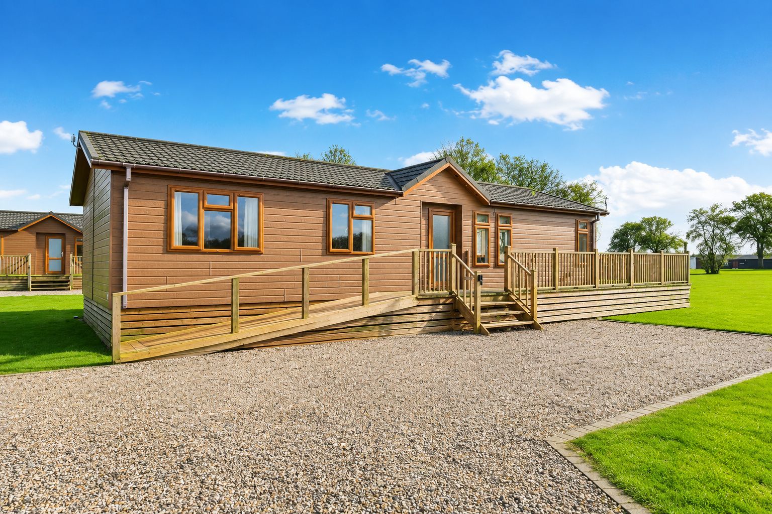A wooden cabin with a gravel driveway, wooden steps, and a grassy lawn.