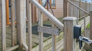 Een houten terras met een bord waarop 'ORCHID' staat en een camera op een statief.