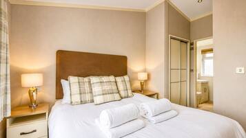 A hotel room with a bed, two bedside lamps, a nightstand, a mirror, and a view of a bathroom.