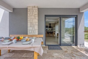 Un coin repas avec une table dressée pour quatre personnes, un mur en pierre et une porte-fenêtre coulissante donnant sur la cuisine.