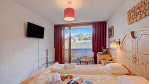 A hotel room with two beds, a television, a view to the outside, a wooden headboard, and a red curtain. - Hotel Relais Alpin Twin Room & Balcony 7 236 summer mode, Les Mosses, Switzerland (Les Mosses)