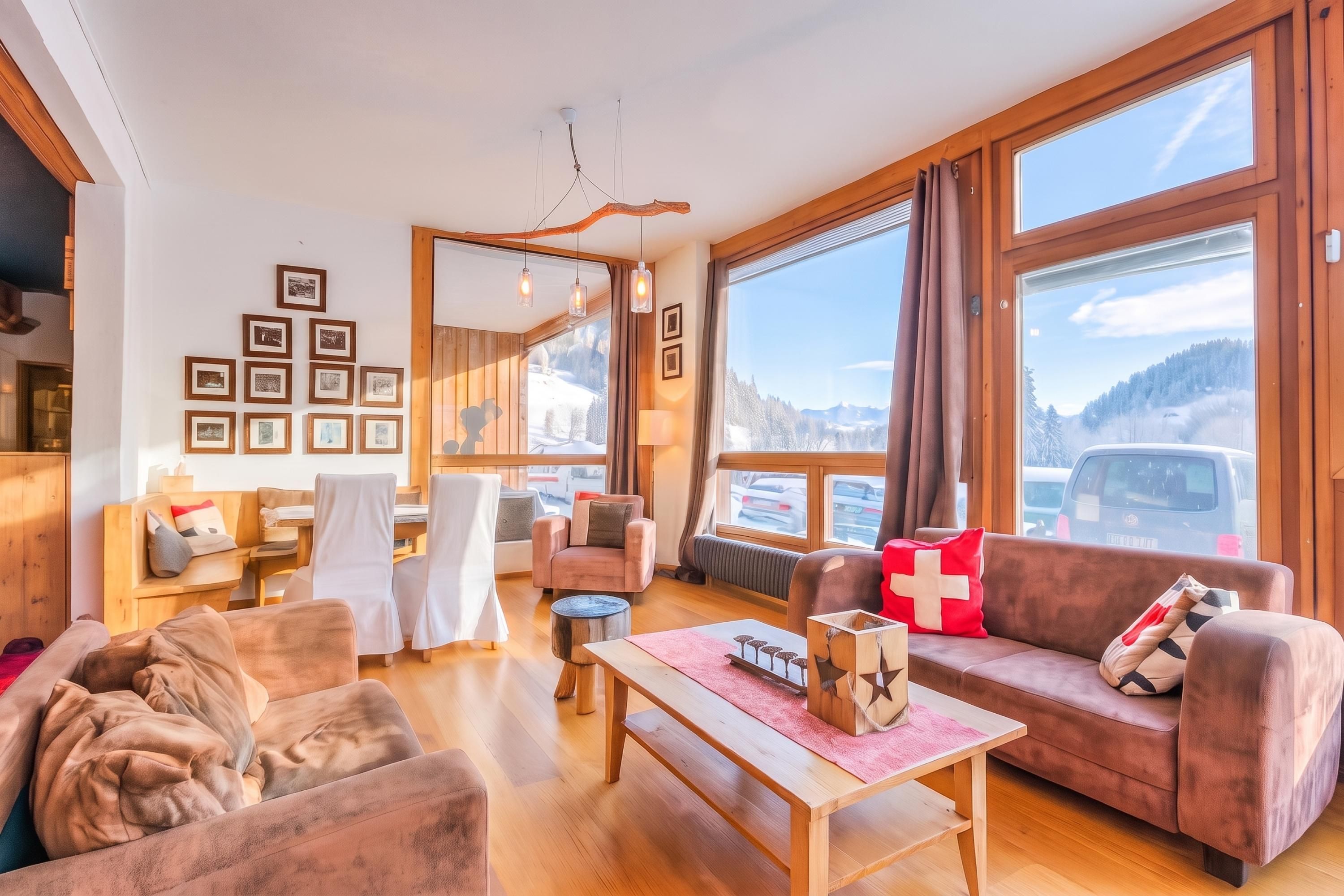 Un salon chaleureux avec un plancher en bois, un canapé, une table basse et une cheminée. Les murs sont ornés de tableaux encadrés, et une fenêtre offre une vue sur les montagnes.