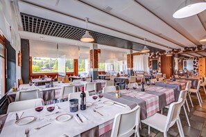 A restaurant with multiple tables set for dining, featuring a modern interior design and large windows offering a view of the outdoors. - Hotel Relais Alpin Twin Room & Balcony 7 236 summer mode, Les Mosses, Switzerland (Les Mosses)
