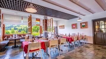 Ein Restaurant mit mehreren Tischen, Stühlen und Blick ins Freie.