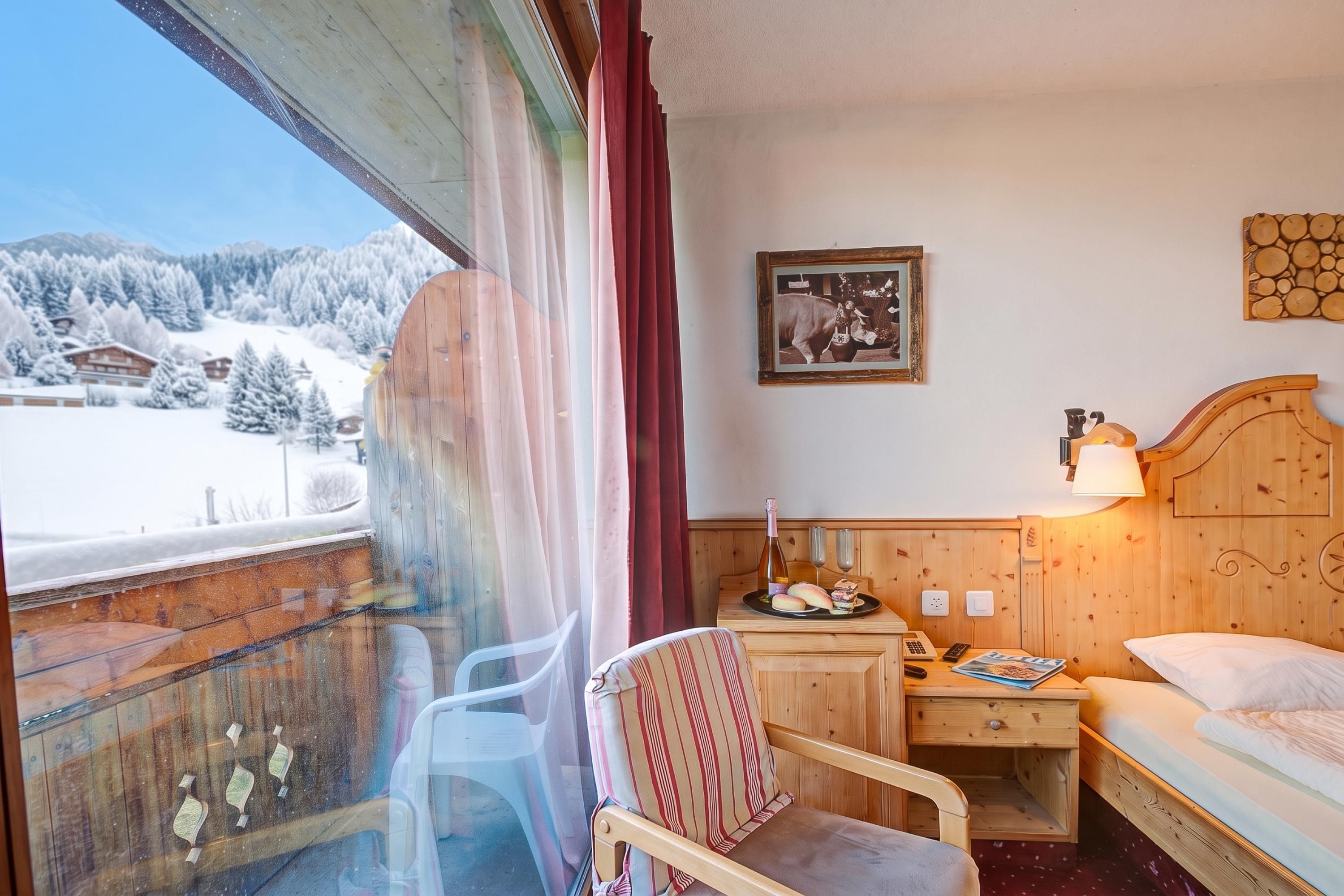 Ein Hotelzimmer mit einem hölzernen Bett, einem Nachttisch mit Lampe, einem Sessel und Blick auf schneebedeckte Berge.