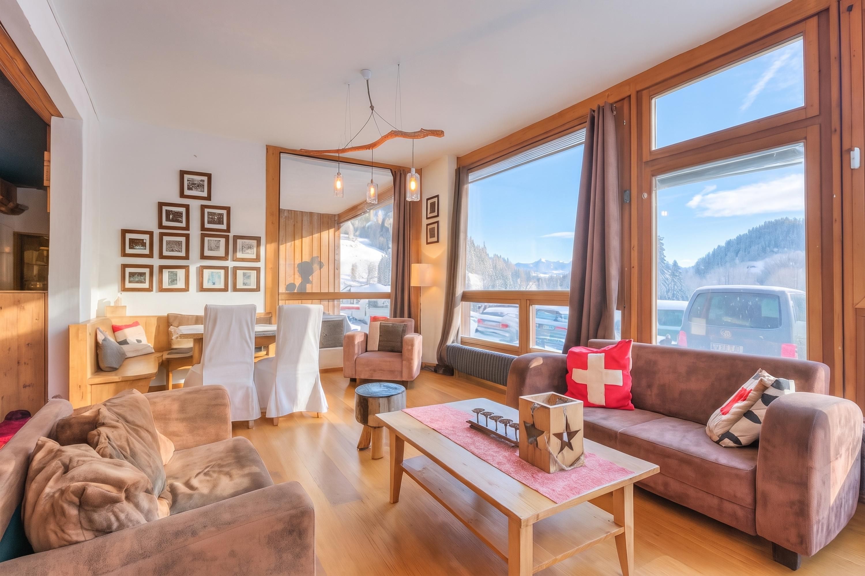 Un salón acogedor con sofá, sillas, una mesa de centro y una chimenea. Amplias ventanas ofrecen vistas al exterior.