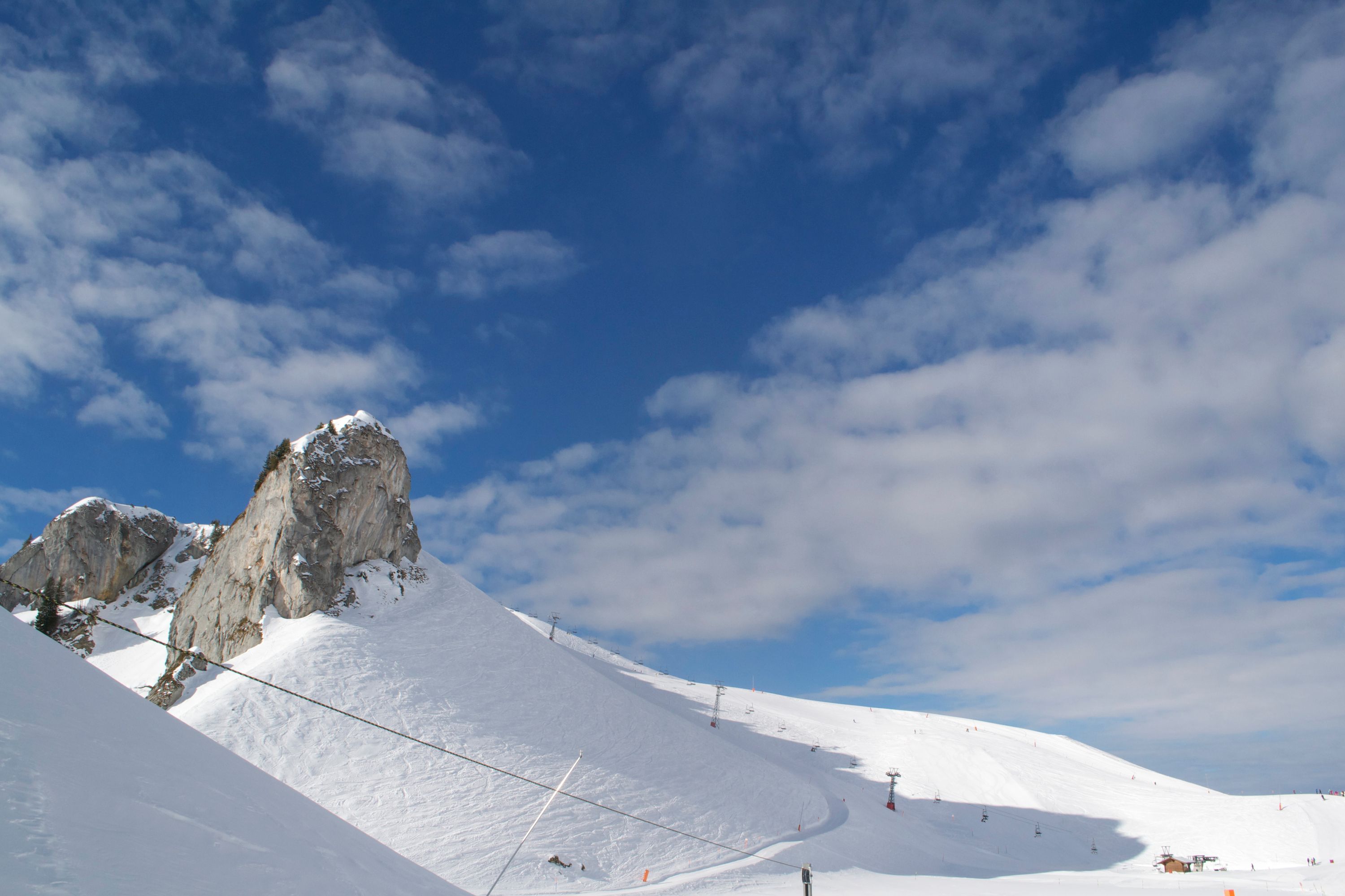 Ein schneebedeckter Berg mit einer Seilbahn, blauem Himmel und felsigen Vorsprüngen.