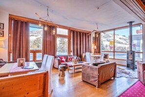 Ein gemütliches Wohnzimmer mit Holzmöbeln, großen Fenstern und einem Kamin.