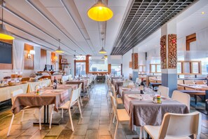 Un restaurant spacieux doté de nombreuses tables et chaises, d’un espace buffet et offrant une vue sur l’extérieur.