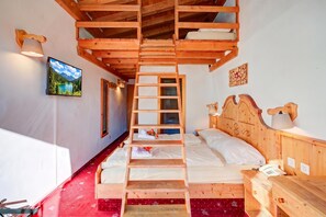 Un lit superposé en bois avec une échelle, un téléviseur fixé au mur et une tête de lit en bois avec une lampe.