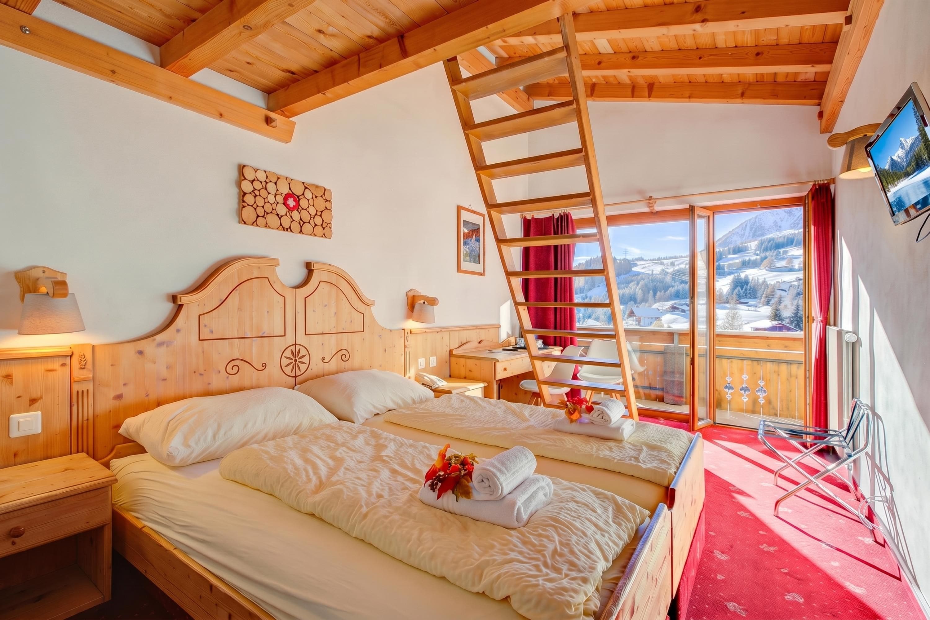 Ein Zimmer in einer Holzhütte mit zwei Betten, einer Leiter, einem Fernseher und Blick auf eine verschneite Landschaft.