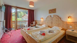 Een kamer met twee houten bedden, een nachtkastje van hout, een stoel, een tafel en uitzicht op een huis door een schuifdeur.