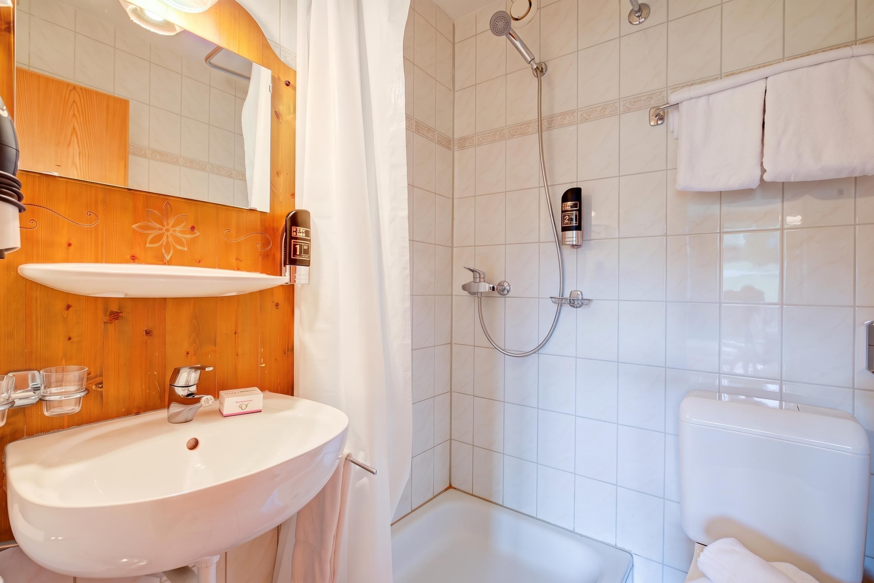 Un baño con un lavabo blanco, paneles de madera, un espejo, una ducha con cabezal de ducha manual y un inodoro.