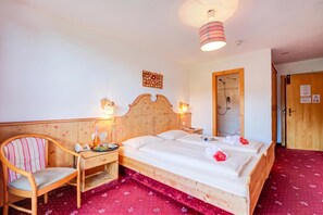 Ein Hotelzimmer mit einem hölzernen Bett, einem Sessel, einem Nachttisch, einer Wandleuchte und einem Duschbereich.