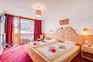 Ein Hotelzimmer mit zwei Betten, einem Holzkopfstück, einem Fenster mit roten Vorhängen, einer Holzwanddekoration und einem kleinen Nachttisch mit einer Lampe.