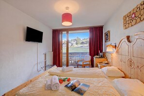 Ein Hotelzimmer mit zwei Betten, einem Fernseher, Blick ins Freie, einem hölzernen Kopfteil und einem roten Vorhang.
