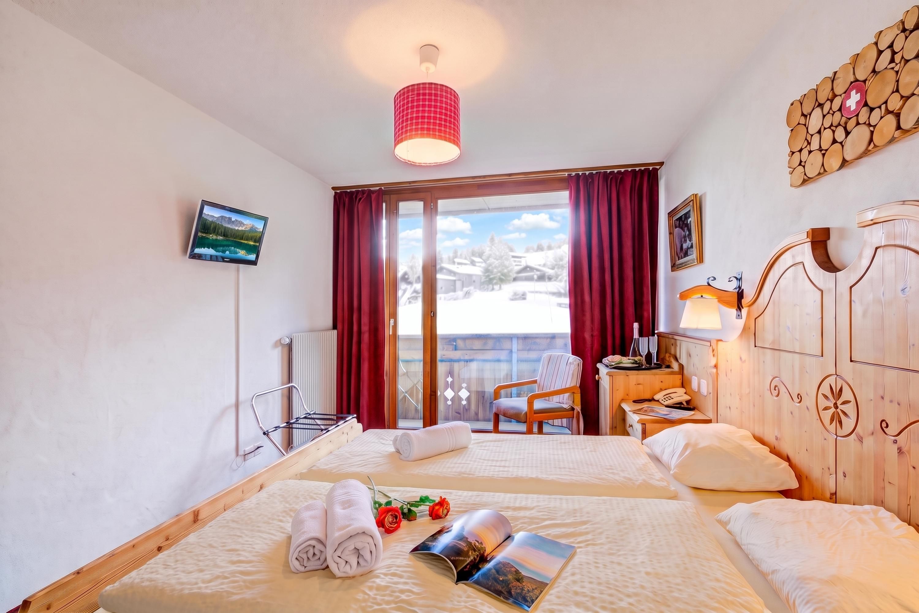 Une chambre d’hôtel avec deux lits, une télévision, une armoire en bois, un bureau avec une lampe et une vue sur un paysage enneigé.