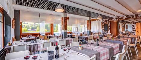 A restaurant with multiple tables set for dining, featuring a modern interior design and large windows offering a view of the outdoors.