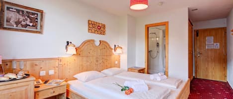 Habitación de hotel con cama de madera, mesitas de noche, un espejo, ducha y alfombra roja.