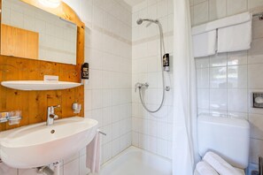 A bathroom with a wooden vanity, a white sink, a mirror, a shower with a handheld showerhead, and a white bathtub. - Hotel Relais Alpin Twin Room & Balcony3 229, Les Mosses, Switzerland (Les Mosses)