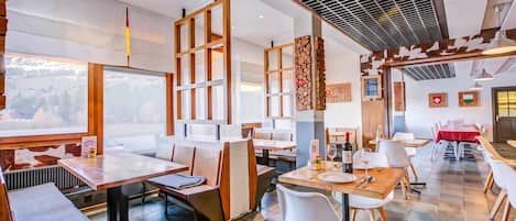 Ein Restaurant mit mehreren Essbereichen, darunter eine U-förmige Sitzgruppe und ein Bereich mit Tischen. Holzstühle und -tische sind vorhanden, und die Decke weist ein gitterartiges Muster auf.