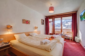 Une chambre d’hôtel avec un lit, des tables de chevet, une fenêtre donnant sur un beau paysage, et une table avec des serviettes et des verres.