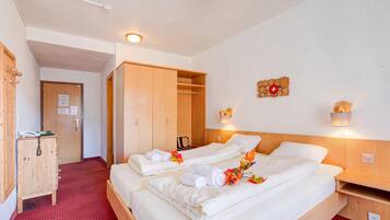 A hotel room with two beds, a wardrobe, a desk, and a wall-mounted light fixture.