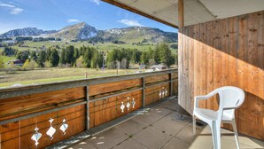 Un balcón con vistas a montañas, una silla de plástico blanca y paneles de madera.