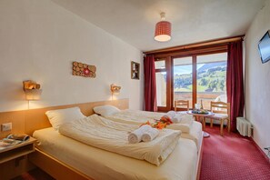 A hotel room with two beds, a small table with a chair, a TV, and a window with a view of the countryside. - Hotel Relais Alpin Twin Room & Balcony9, Les Mosses, Switzerland (Les Mosses)