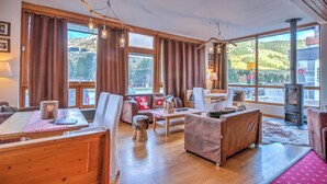 Una sala de estar acogedora con una mesa de madera, sofá y sillas, ventanas amplias con cortinas y una chimenea.