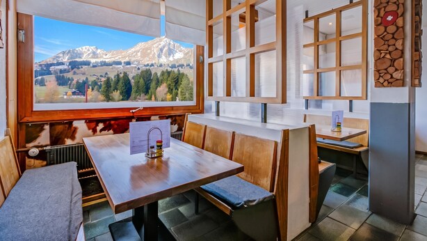 Un restaurante acogedor con mobiliario de madera, un amplio ventanal que ofrece vistas a la montaña y un menú sobre la mesa.