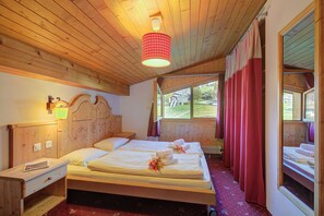 Una habitación de madera con dos camas, una mesita de noche, una lámpara y una ventana con cortinas.
