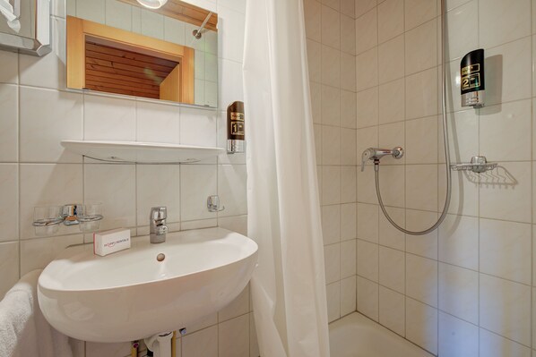 Ein Badezimmer mit weißem Waschbecken, einem Spiegel, einer Dusche und einem Handtuchhalter.