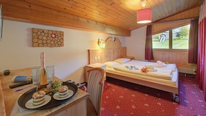 A wooden-paneled room with a bed, a desk with a tray of desserts, and a window with curtains.